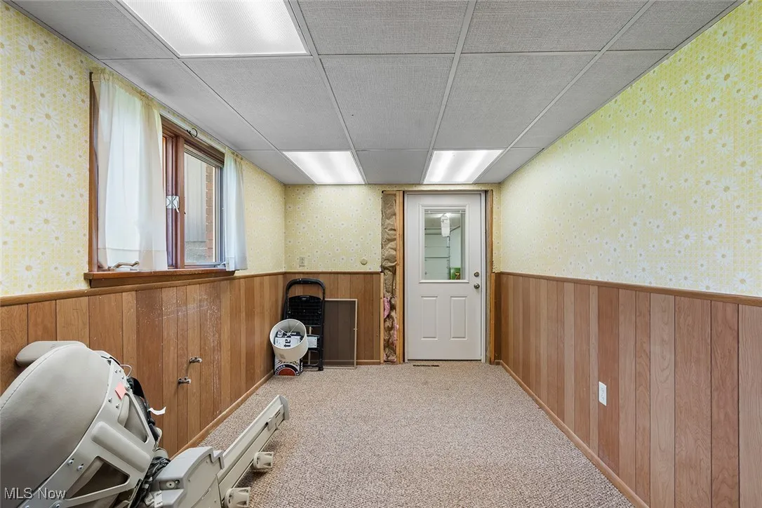 Doorway to outside featuring wooden walls, wainscoting, wallpapered walls, and carpet