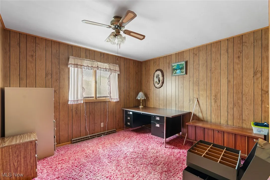 Office space featuring a baseboard heating unit, a ceiling fan, wood walls, and carpet flooring