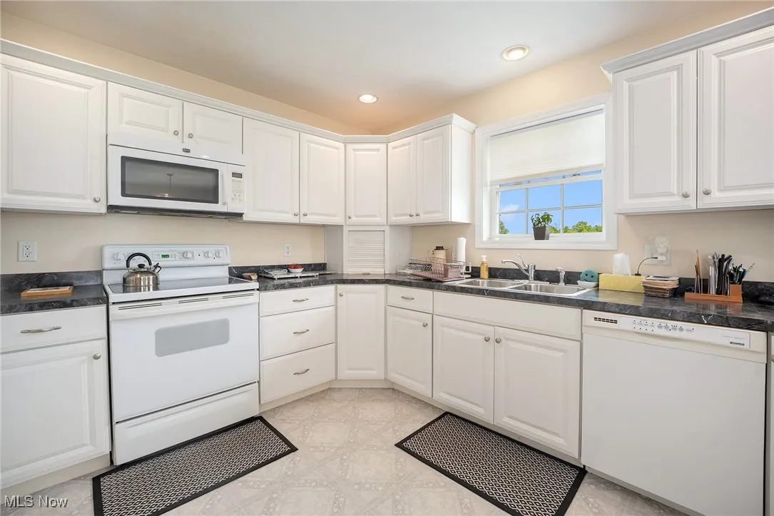Kitchen with white appliances, white cabinets, dark countertops, and recessed lighting