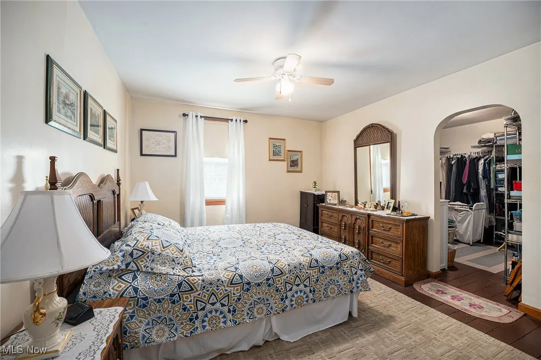 Bedroom featuring a spacious closet, arched walkways, wood finished floors, a ceiling fan, and a closet