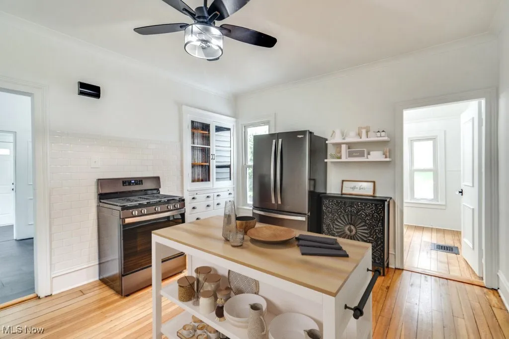 Kitchen with appliances with stainless steel finishes, light wood-type flooring, ornamental molding, and a ceiling fan