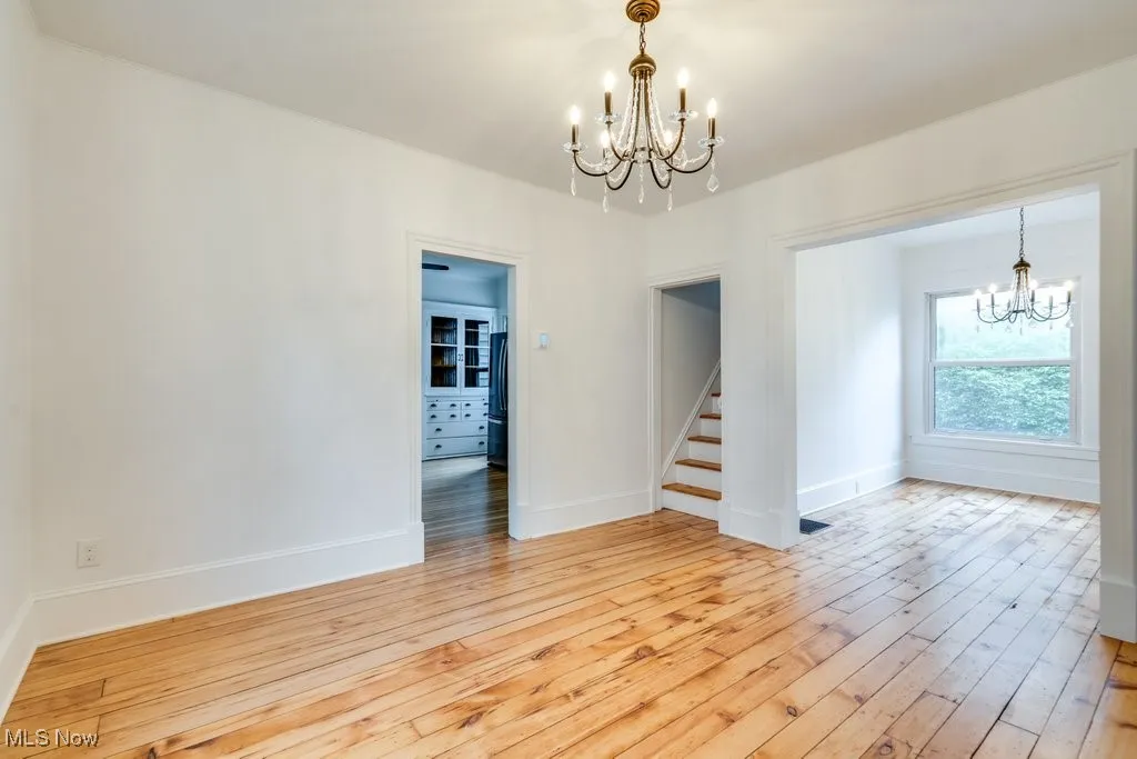 Unfurnished room featuring a chandelier, light wood finished floors, and stairway