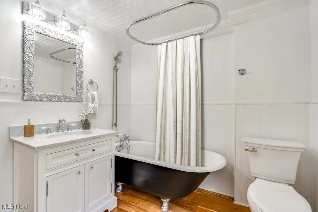 Full bathroom with vanity, shower / bath combo, a wainscoted wall, wood finished floors, and a decorative wall