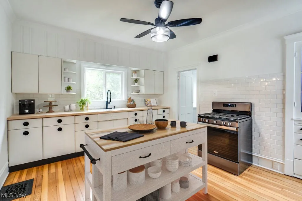 Kitchen with stainless steel gas stove, open shelves, decorative backsplash, light wood finished floors, and crown molding