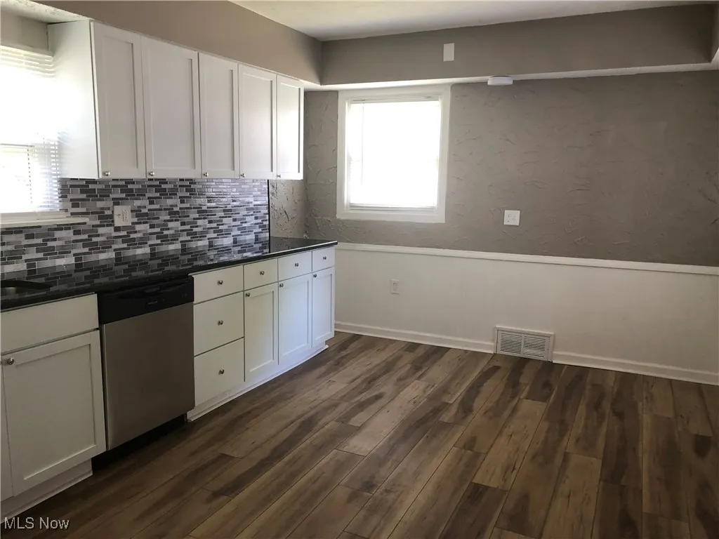 Kitchen with dishwasher, dark countertops, tasteful backsplash, and white cabinetry