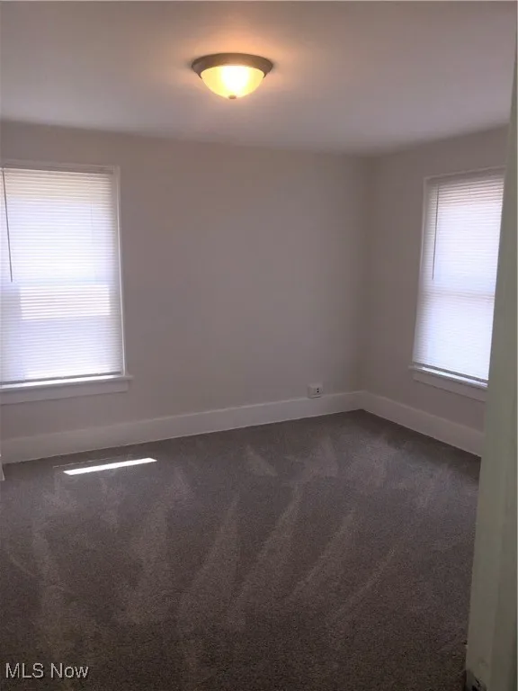 Unfurnished room featuring dark colored carpet and baseboards