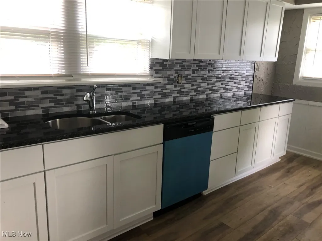 Kitchen with dishwashing machine, backsplash, dark wood-style flooring, and white cabinetry