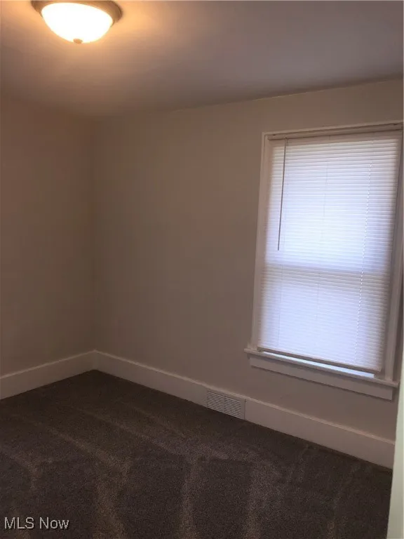 Empty room featuring dark colored carpet and baseboards
