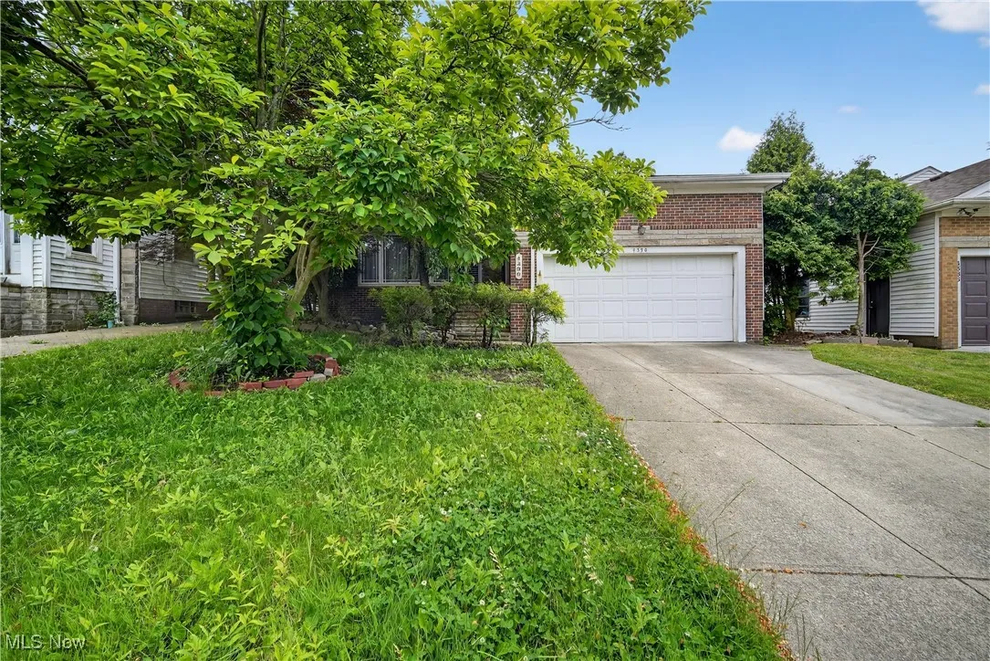Obstructed view of property with driveway, brick siding, a garage, and a front yard