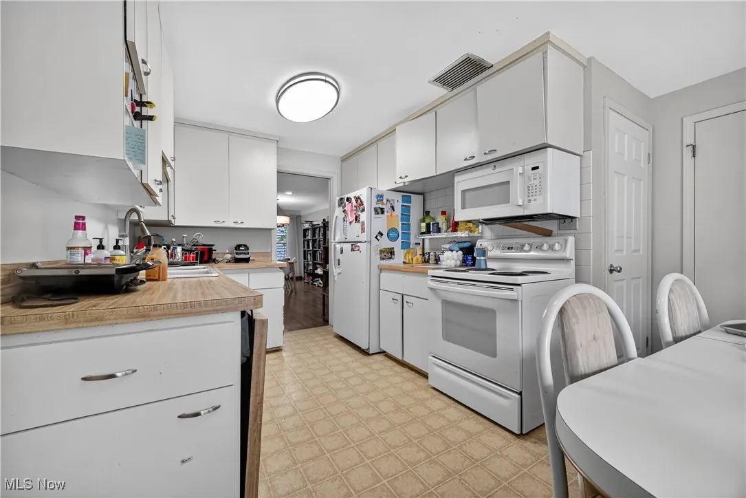 Kitchen featuring white appliances, light flooring, light countertops, and white cabinetry