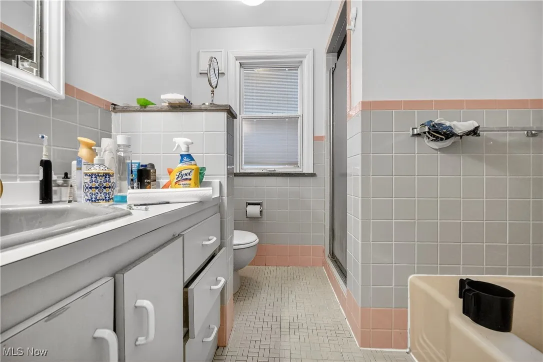 Full bathroom with tile walls, vanity, a stall shower, a wainscoted wall, and a bathtub