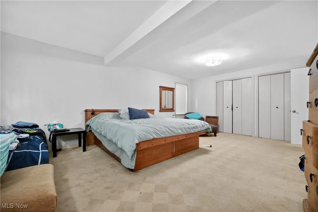 Bedroom with light colored carpet, two closets, and beamed ceiling