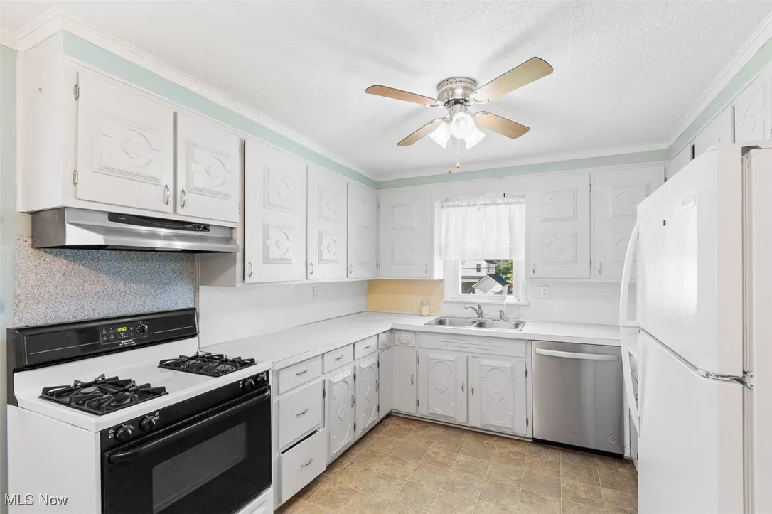 Kitchen featuring white appliances, under cabinet range hood, a ceiling fan, ornamental molding, and light countertops