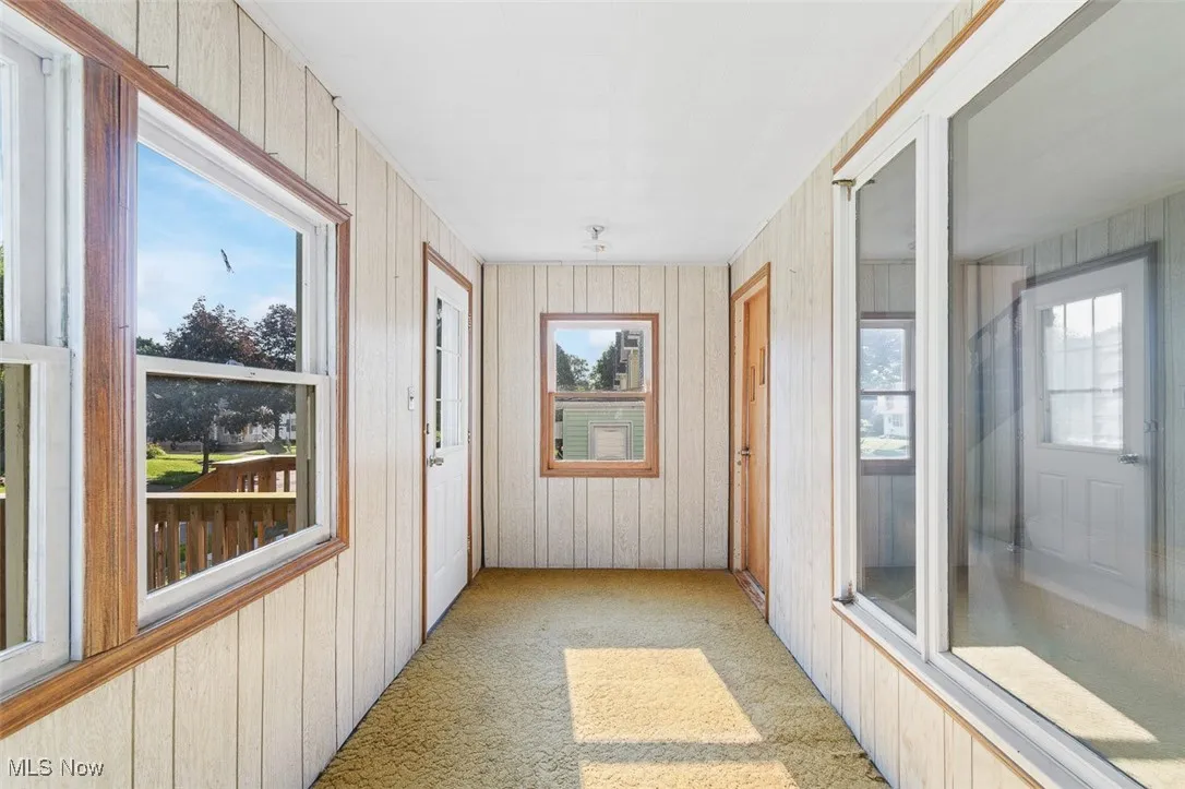 Unfurnished sunroom with plenty of natural light, carpet floors, and wood walls