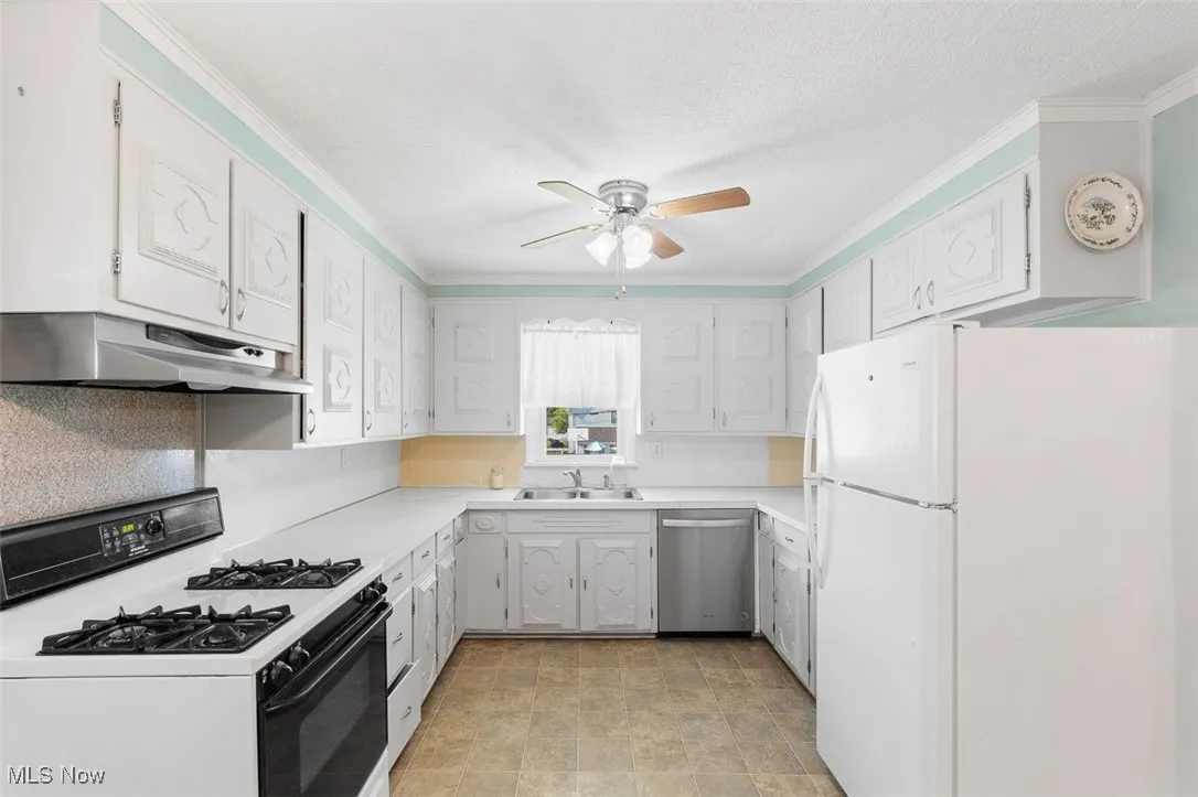 Kitchen with freestanding refrigerator, range with gas stovetop, under cabinet range hood, dishwasher, and a ceiling fan