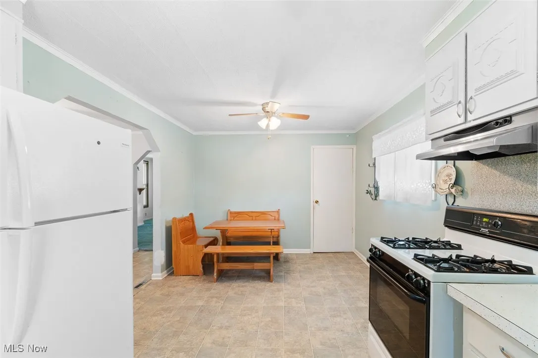 Kitchen featuring freestanding refrigerator, black gas range, ornamental molding, under cabinet range hood, and ceiling fan
