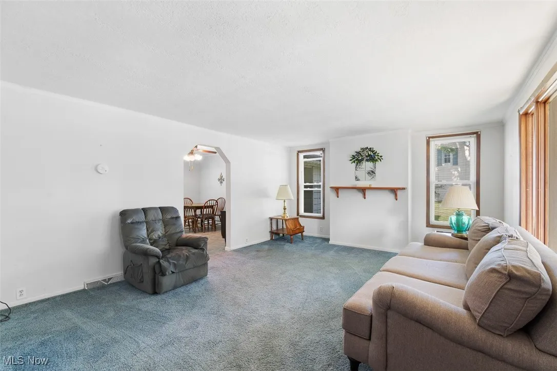 Carpeted living area featuring arched walkways and a textured ceiling