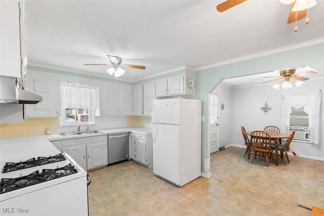 Kitchen featuring white appliances, a ceiling fan, crown molding, light countertops, and arched walkways