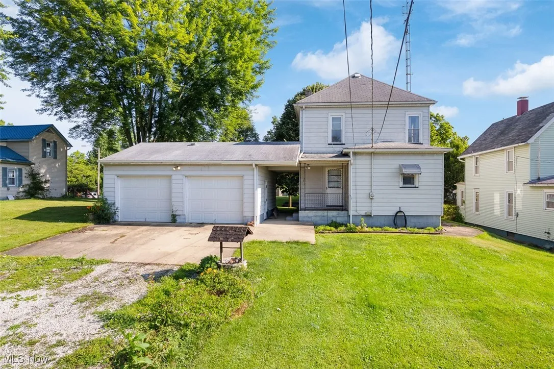 Back of house with driveway, an attached garage, and a lawn