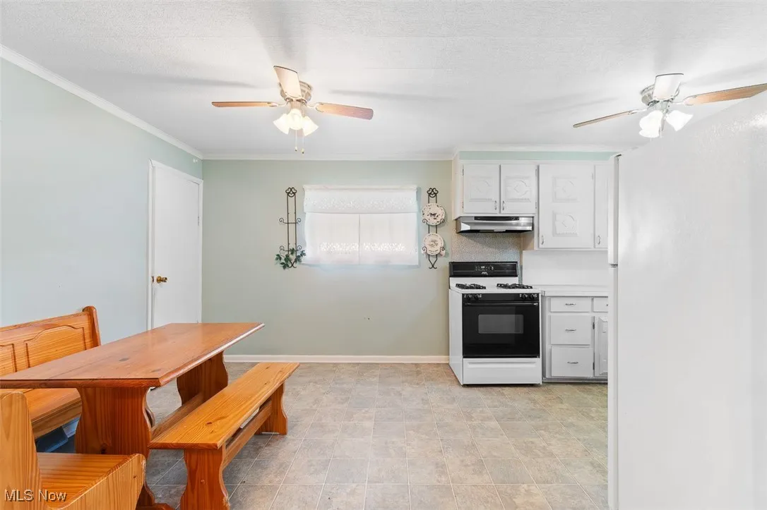 Kitchen featuring white gas stove, under cabinet range hood, ceiling fan, white cabinetry, and ornamental molding
