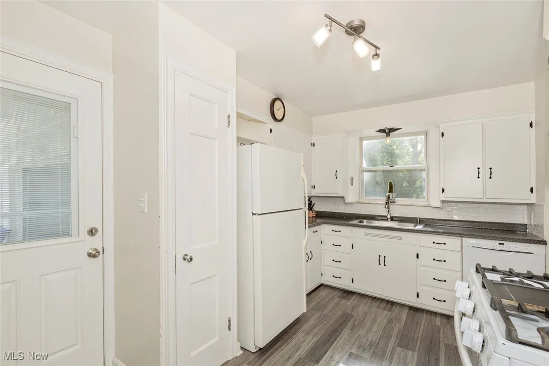 Kitchen featuring white appliances, dark countertops, dark wood-style floors, white cabinetry, and decorative backsplash
