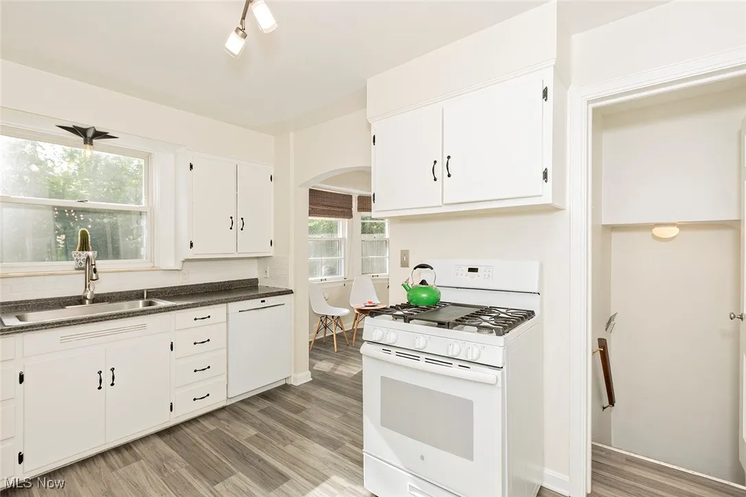 Kitchen with white appliances, arched walkways, dark countertops, white cabinets, and light wood finished floors