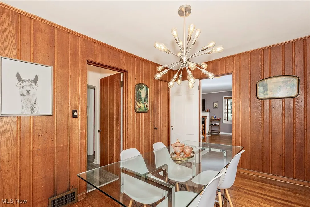 Dining space with a chandelier, wood finished floors, wood walls, and ornamental molding