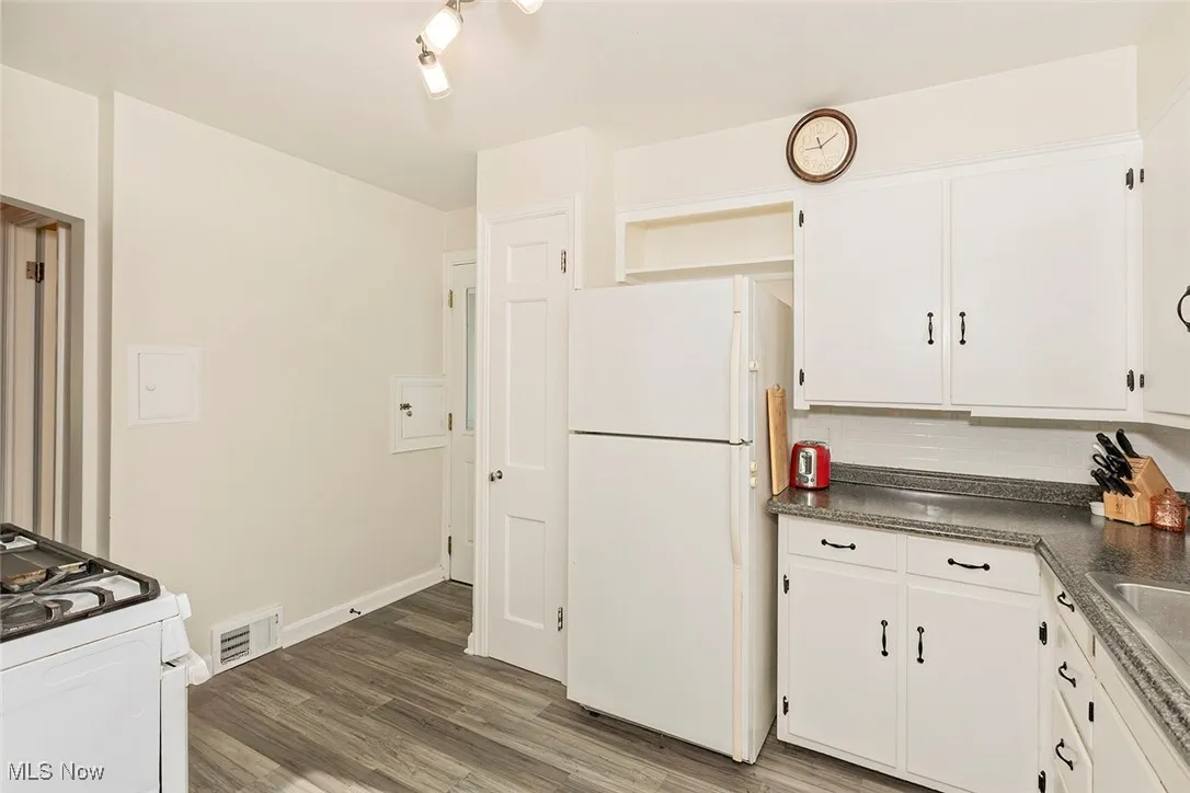 Kitchen with white appliances, white cabinets, dark countertops, light wood finished floors, and decorative backsplash