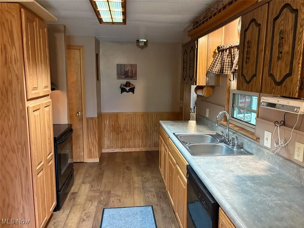 Kitchen featuring black appliances, a wainscoted wall, wood finished floors, light countertops, and wood walls