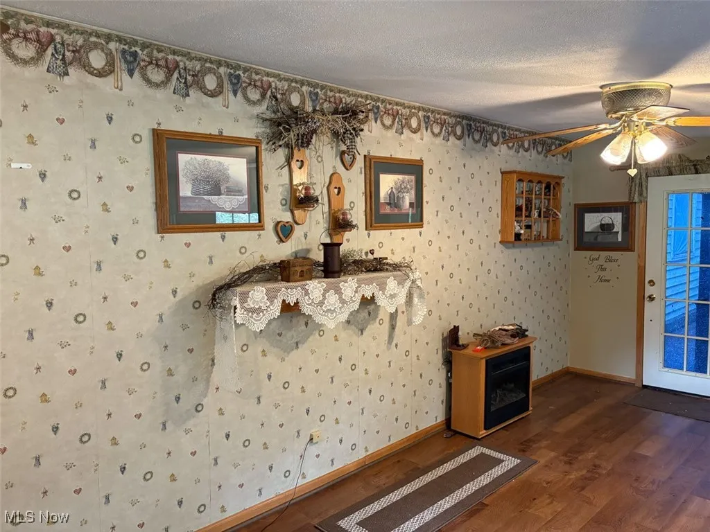 Living room with wood finished floors, ceiling fan, wallpapered walls, and a textured ceiling