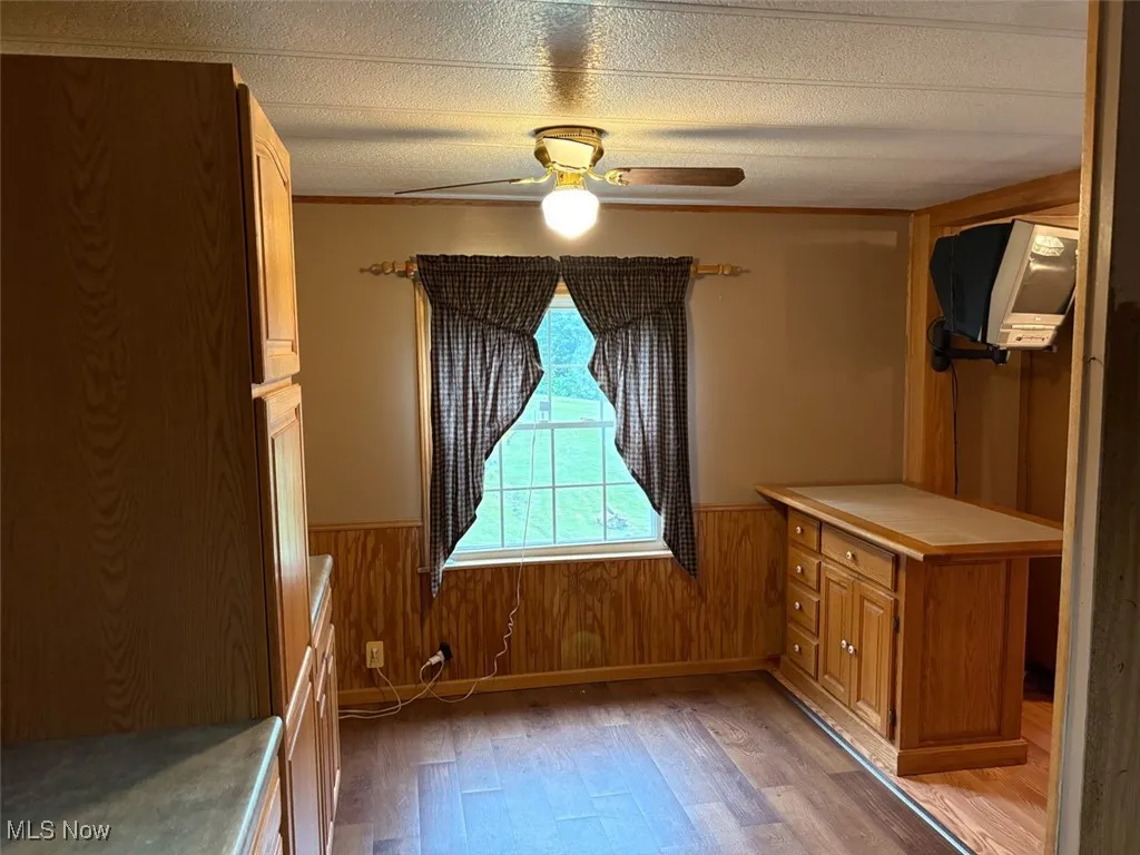 Kitchen featuring light wood-type flooring, wainscoting, a ceiling fan, a textured ceiling, and wood walls