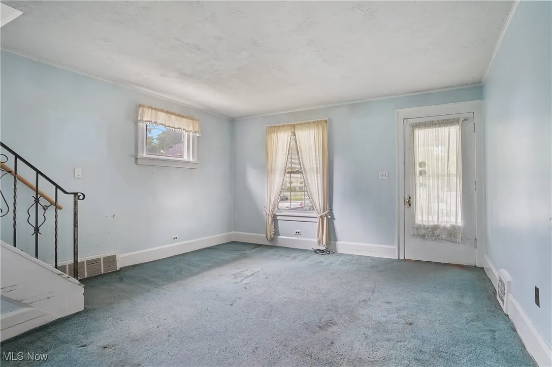 Unfurnished living room with a textured ceiling, carpet, stairway, and ornamental molding