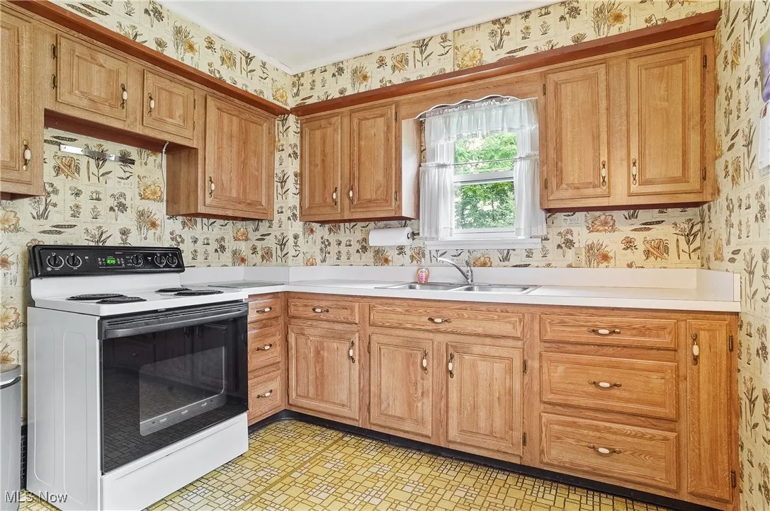 Kitchen with white range with electric stovetop, wallpapered walls, light countertops, and brown cabinets