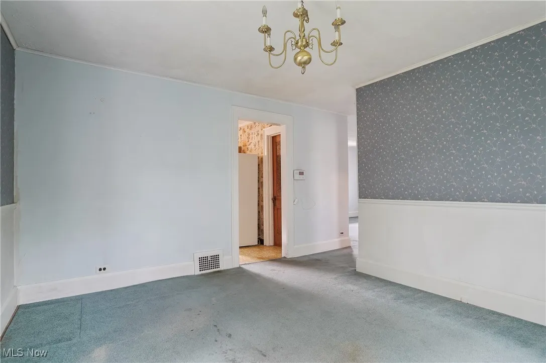 Carpeted empty room featuring a chandelier, wallpapered walls, and ornamental molding