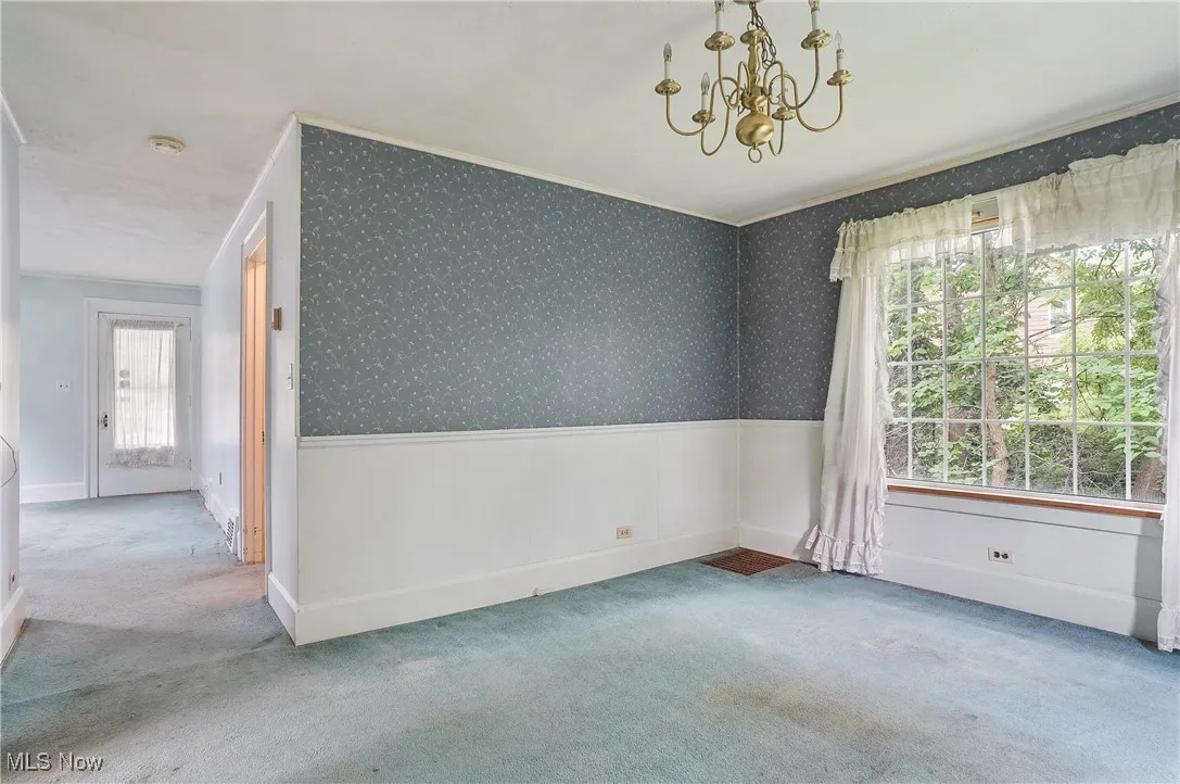 Carpeted empty room featuring a chandelier, plenty of natural light, crown molding, a wainscoted wall, and wallpapered walls