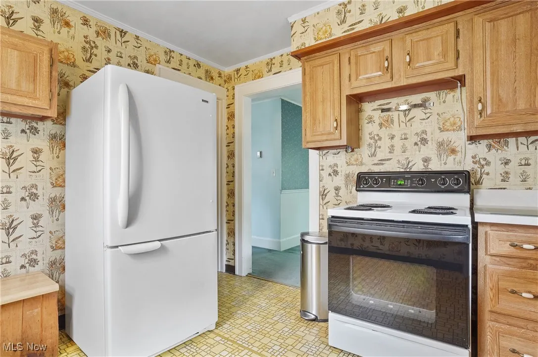 Kitchen with white appliances, wallpapered walls, crown molding, light countertops, and light flooring