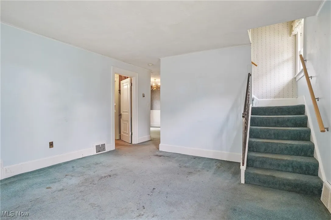 Unfurnished living room featuring stairway and carpet