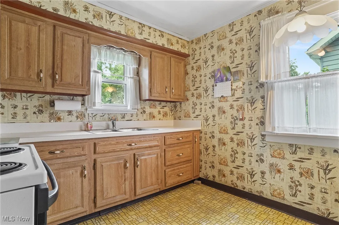 Kitchen with wallpapered walls, electric stove, light floors, light countertops, and brown cabinetry
