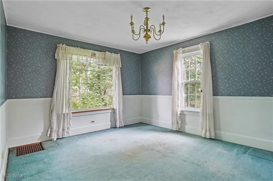 Unfurnished room featuring a chandelier, carpet flooring, ornamental molding, and wallpapered walls