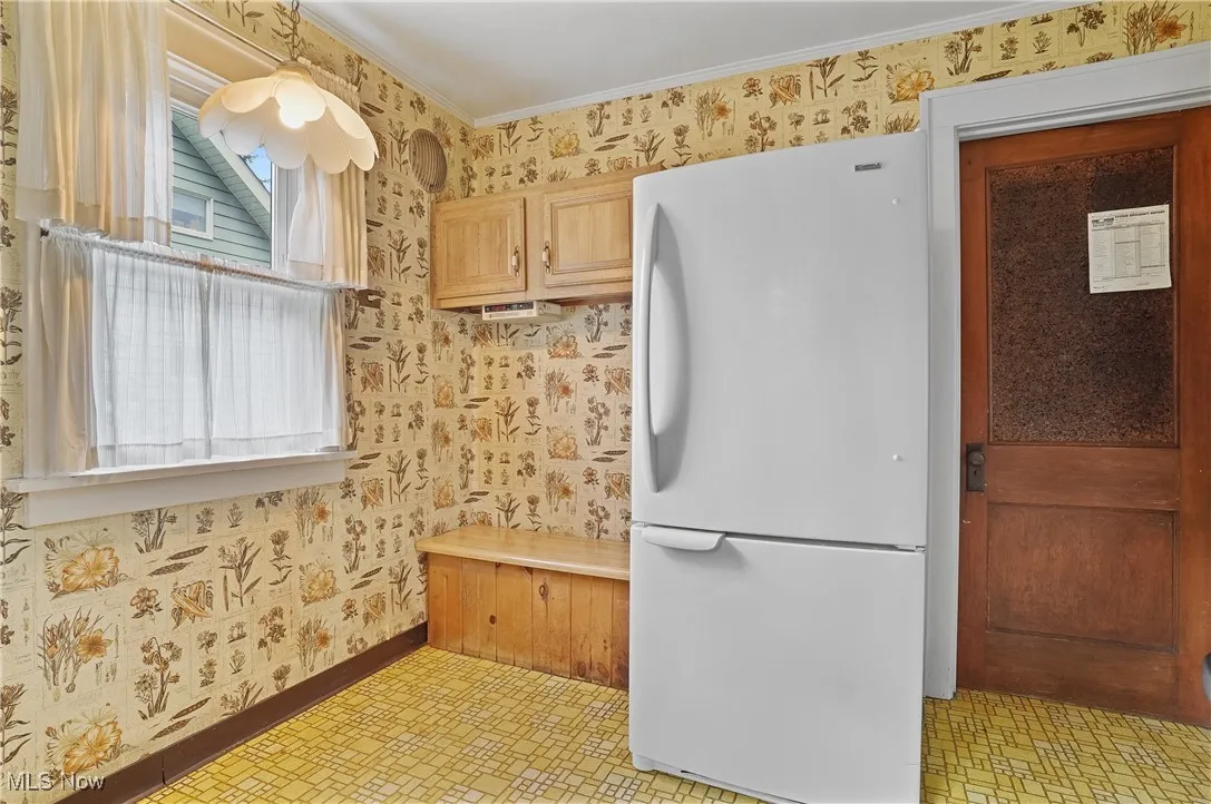 Kitchen featuring freestanding refrigerator, wallpapered walls, light floors, and crown molding