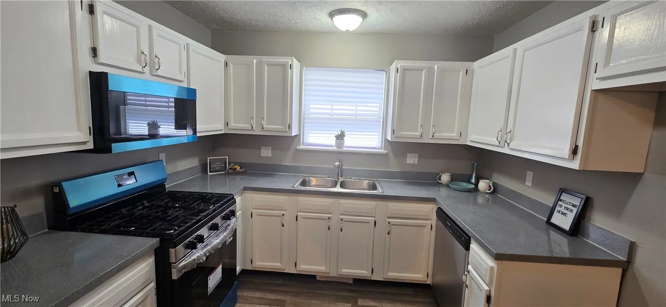 Kitchen featuring stainless steel appliances, white cabinets, a textured ceiling, and dark wood-style floors