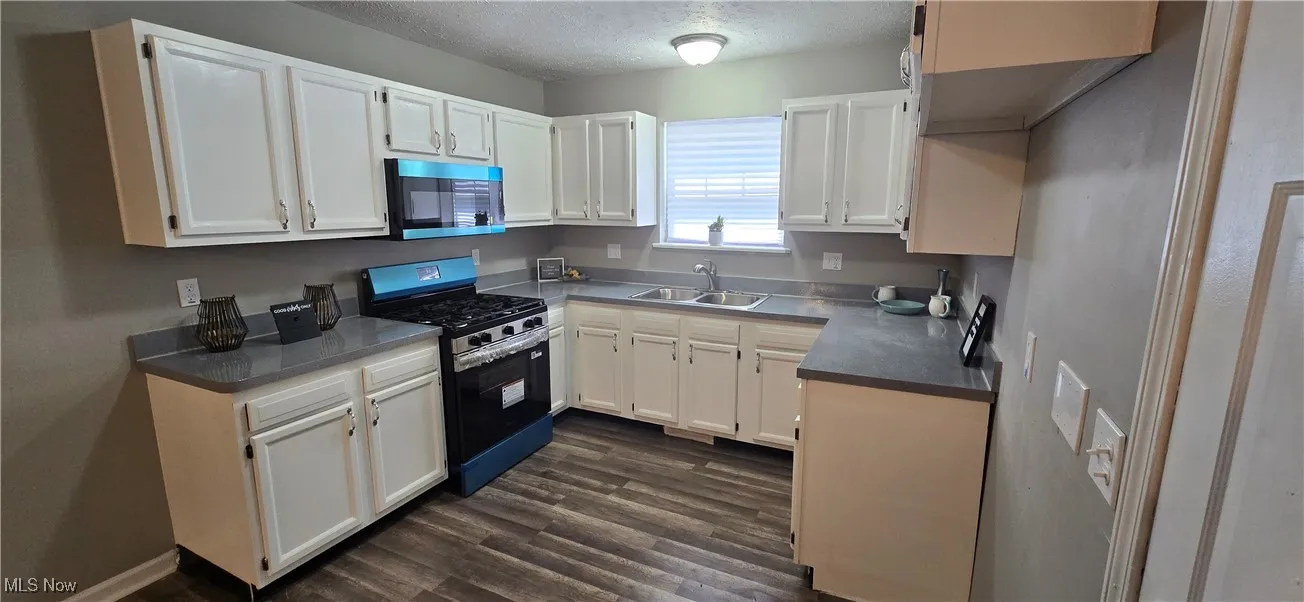 Kitchen featuring stainless steel appliances, dark wood-style floors, white cabinets, a textured ceiling, and dark countertops