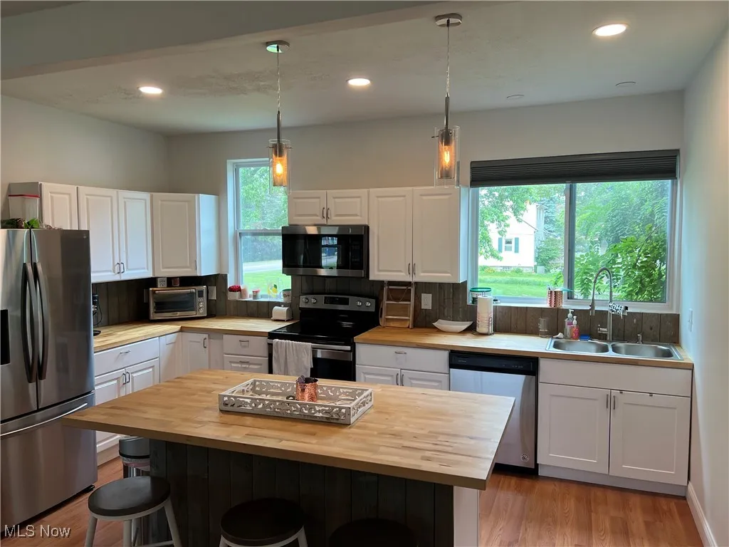 Kitchen featuring stainless steel appliances, butcher block countertops, a kitchen bar, white cabinets