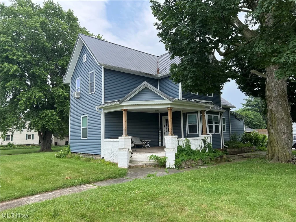View of front of property with covered porch, a front yard, and a metal roof