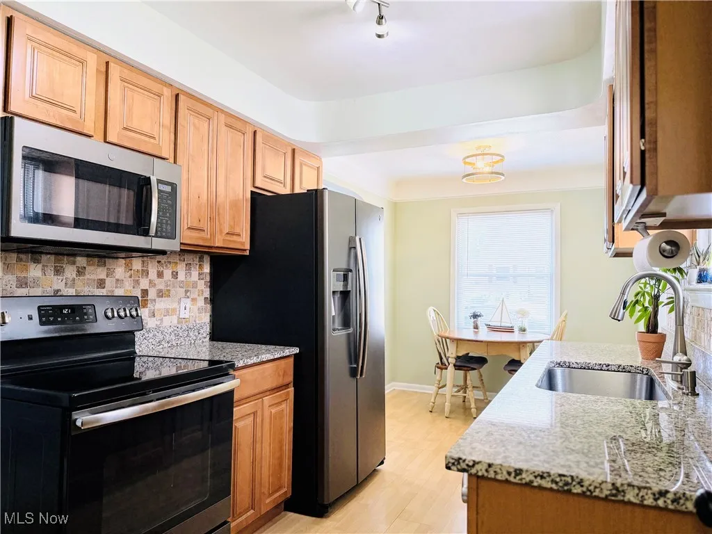 Kitchen featuring appliances with stainless steel finishes, light wood-type flooring, decorative backsplash, and light stone counters