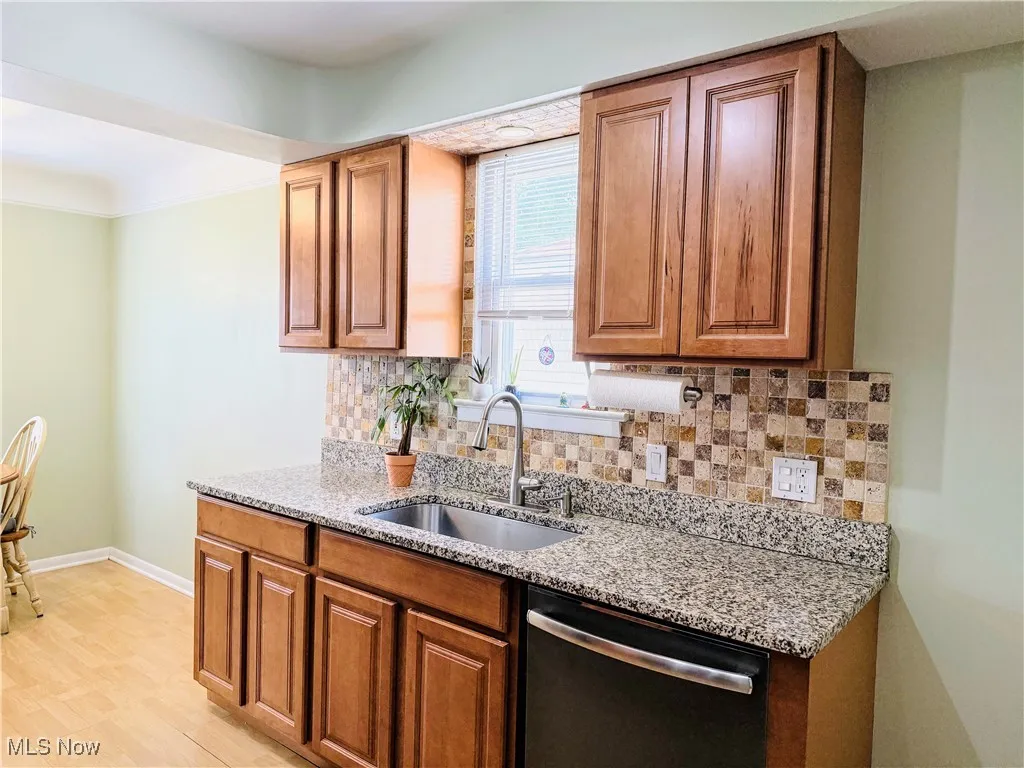 Kitchen with dishwasher, light stone counters, brown cabinets, and tasteful backsplash