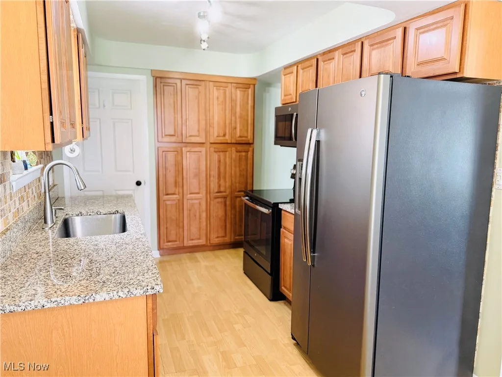 Kitchen featuring stainless steel appliances, light wood finished floors, backsplash, and light stone counters