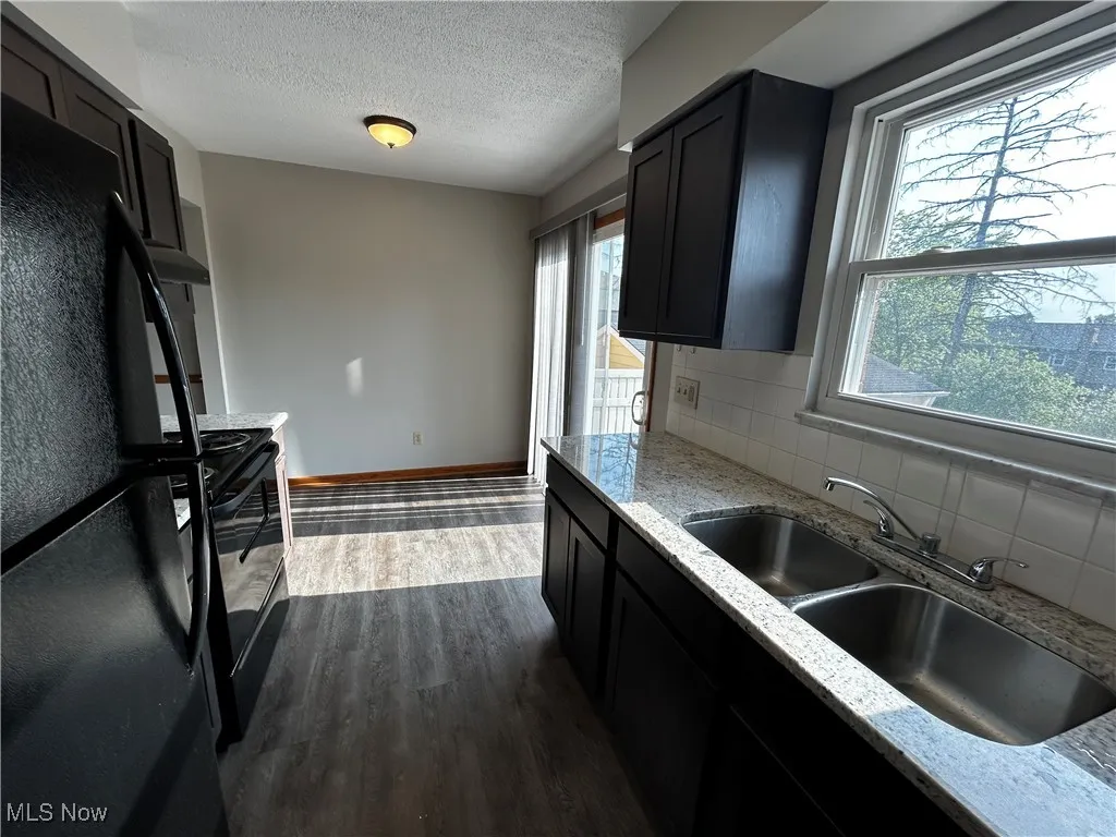 Kitchen with black appliances, dark wood finished floors, healthy amount of natural light, decorative backsplash, and a textured ceiling