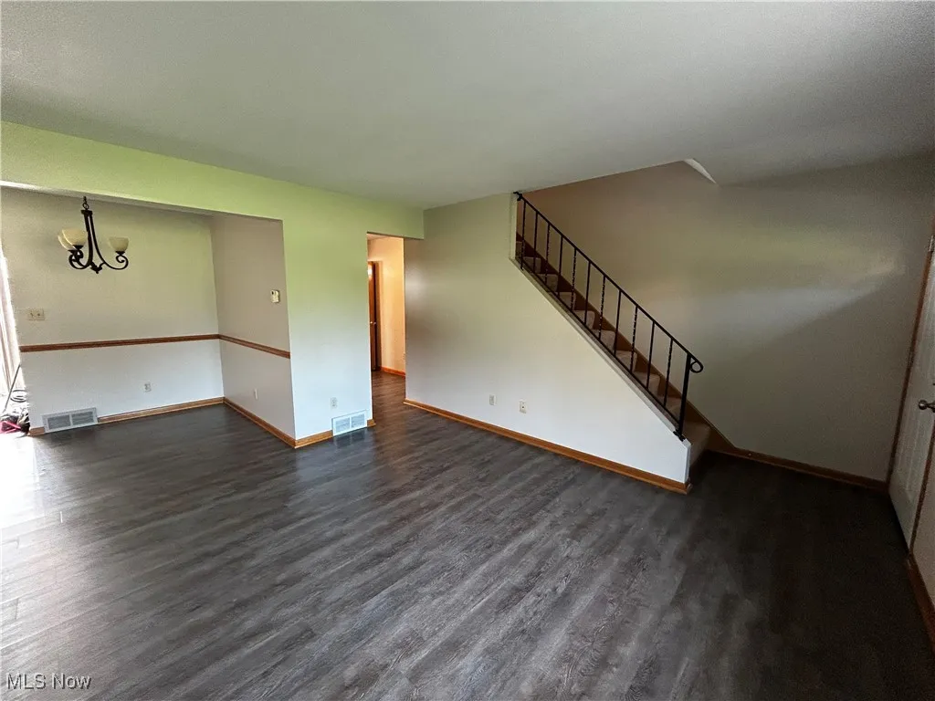 Unfurnished living room featuring dark wood-style flooring, stairs, and a chandelier