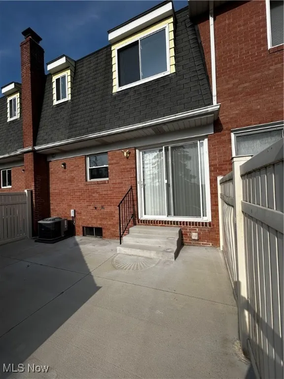 Rear view of house with entry steps, a shingled roof, brick siding, a patio area, and a chimney